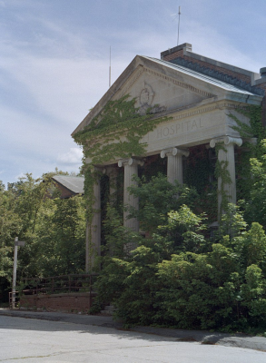 An abandoned neoclassical hospital building at Mansfield Training School covered in vines and bushes