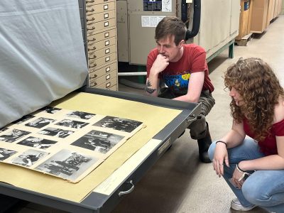 Matt Iannantuoni and Jess Gallagher squat to closely observe black and white archived photos from MTS